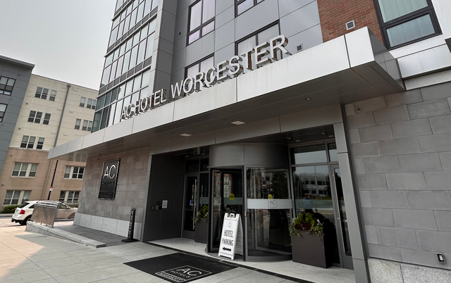 The front entrance of the AC Hotel Worcester, which is ground floor with no steps, with either a rotating door or standard doors to either side. It is on the corner of the block with a nice wide sidewalk.