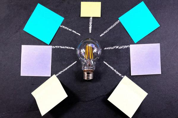 A lightbulb lies in the center of six blank post-it notes.
