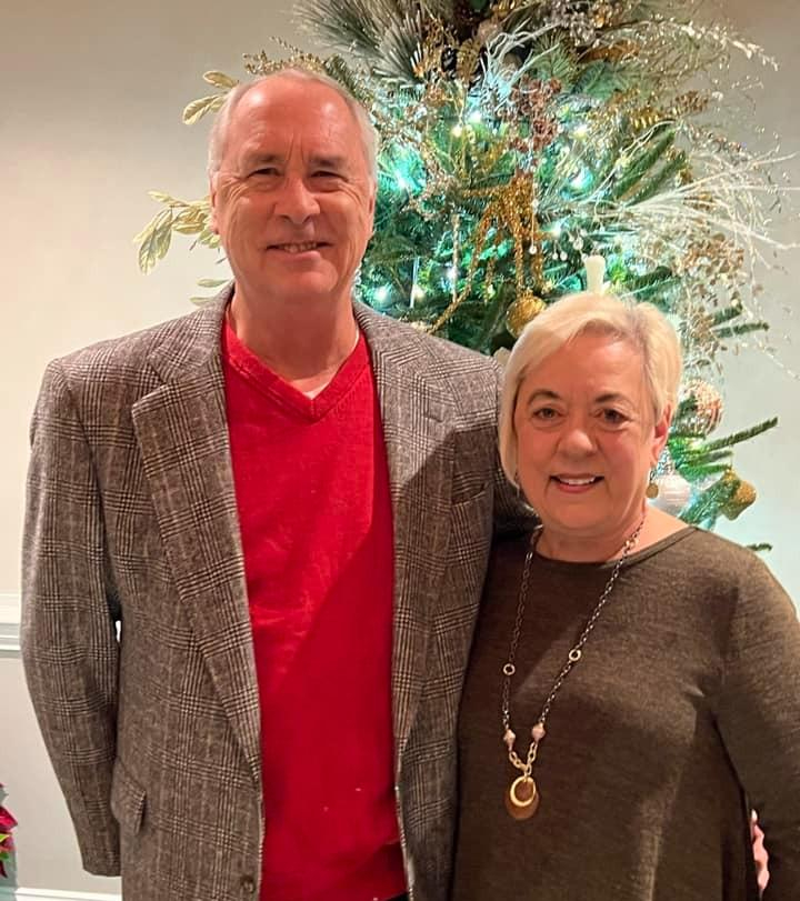 Photo of John and Laura smiling in front of a Christmas tree.