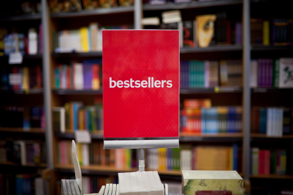 A sign reading Bestsellers on a table of books, with bookshelves in the background.