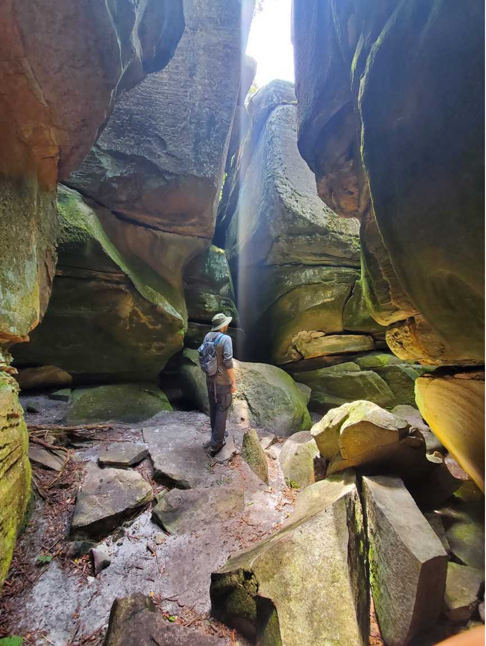 George stands with his back to the camera in the middle of a cave looking up.