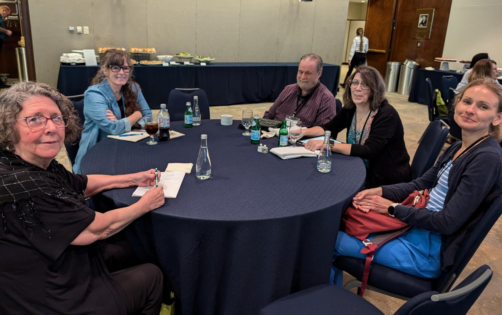 Five NLS conference attendees sit at a round table eagerly anticipating the next session.