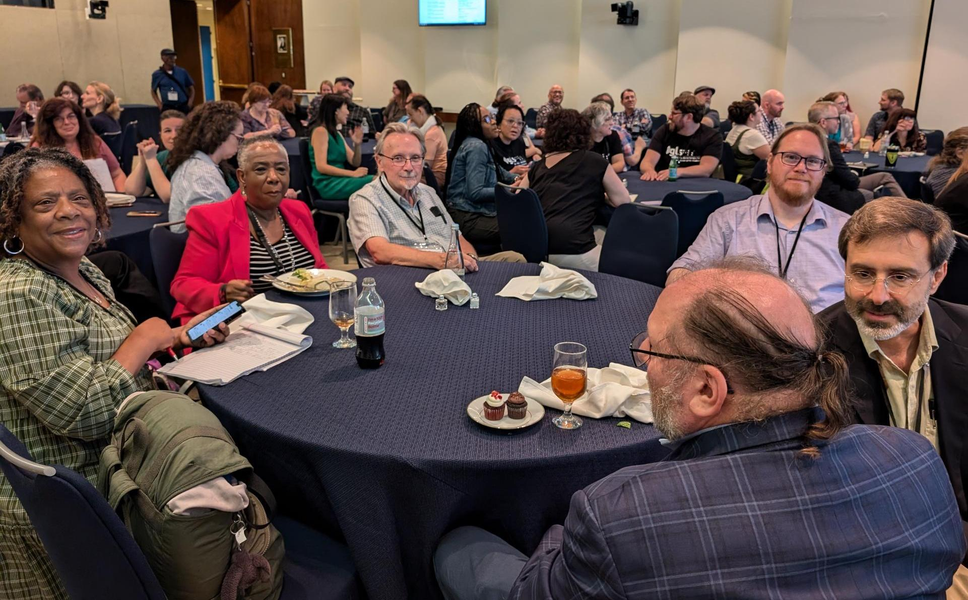 6 NLS conference attendees smile and chat around a table after enjoying the Keystone provided lunch. 