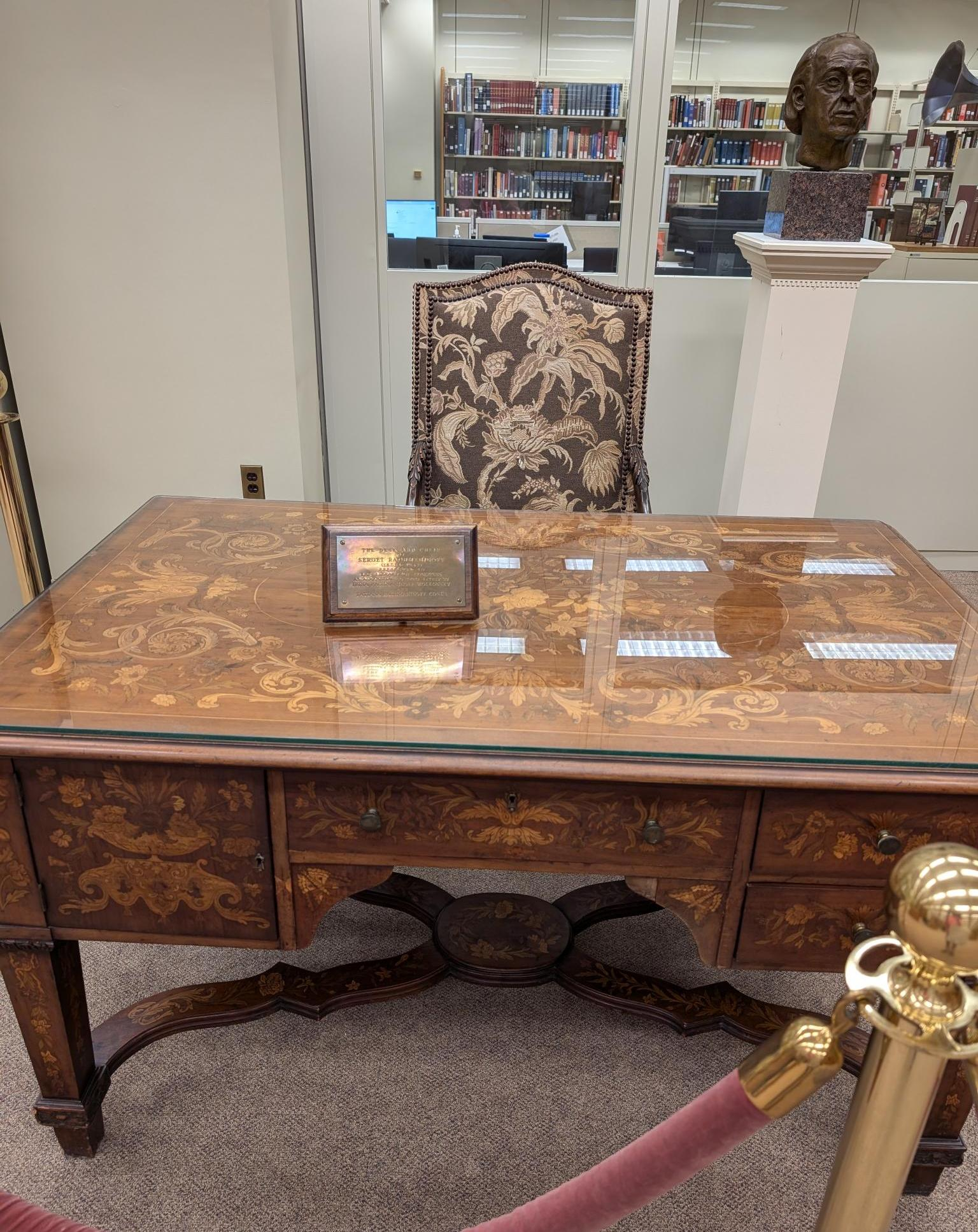 Rachmaninov's desk is made of ornate inlaid wood, with even the legs and supports across the bottom of the desk being intricately decorated. It stands here with a plaque on the glass-protected surface, with a chair upholstered to match and a bust of the composer, all behind a velvet rope.