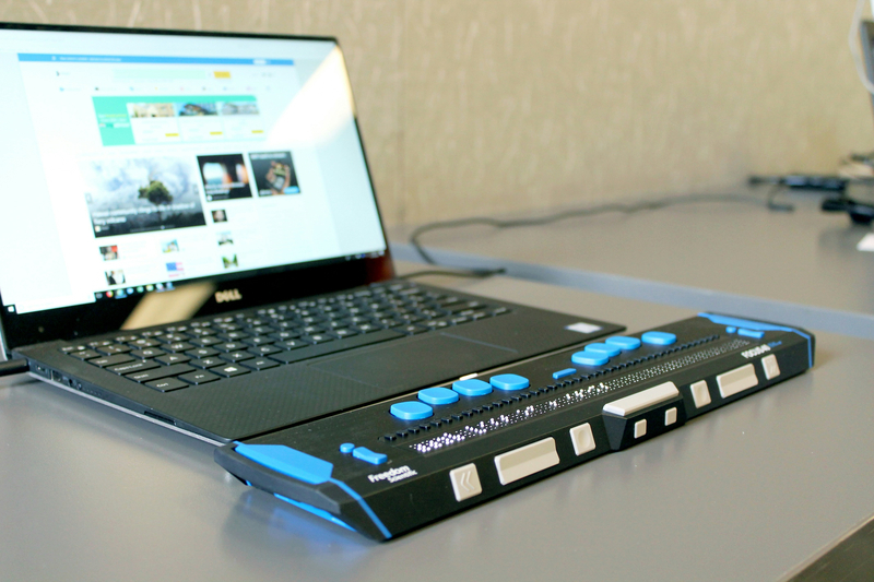 An open laptop with an attached braille reader.
