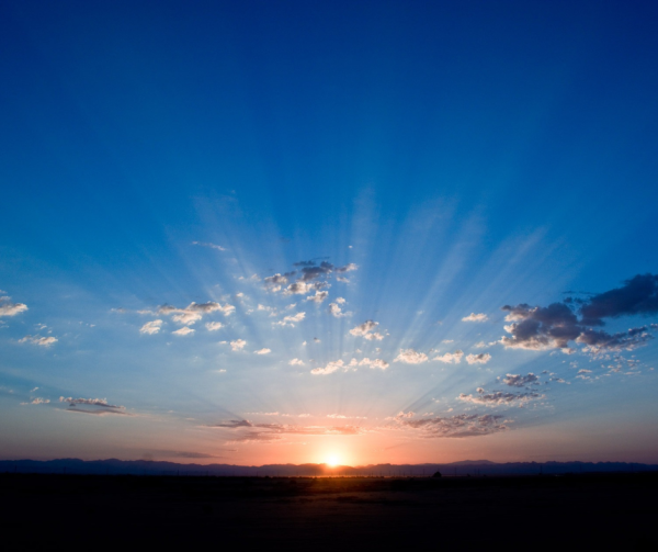 Photo of a sunrise with a bright blue sky and rays of light.
